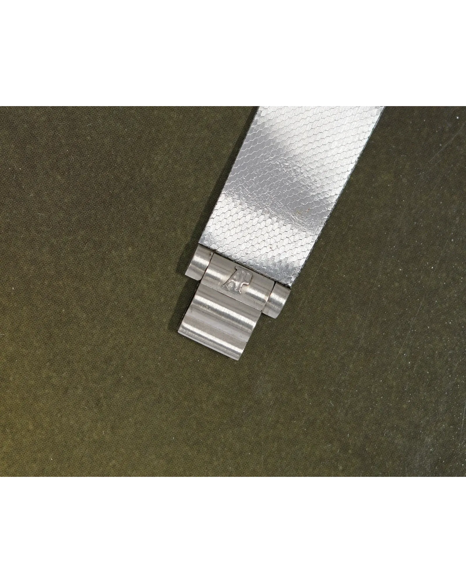 Flat-lay shot of a steel bracelet watch with silver reflective dial on olive fabric surface.