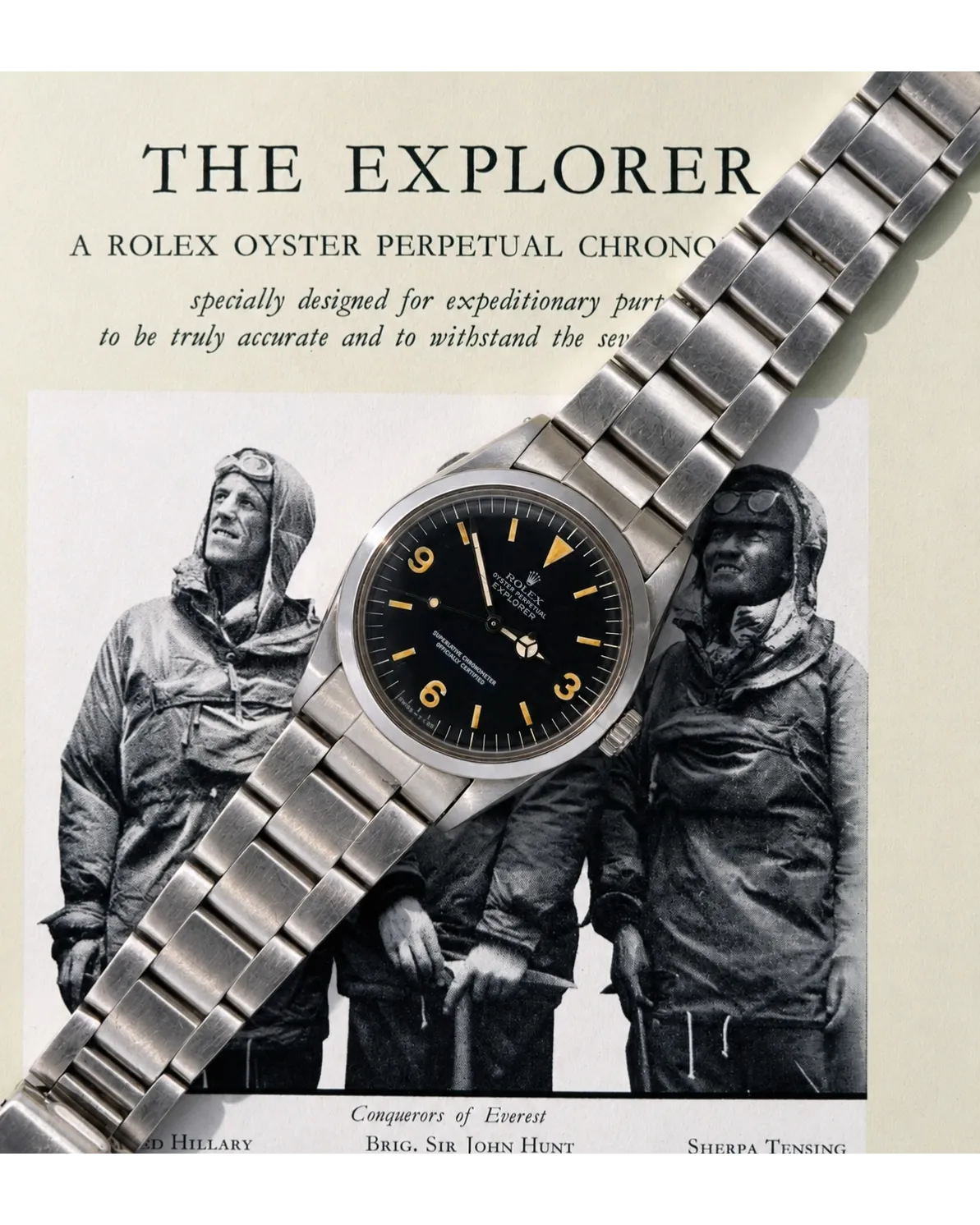 Flat-lay shot of Rolex Explorer with black dial, Arabic numerals, warm patina, and Oyster bracelet on vintage advertisement.