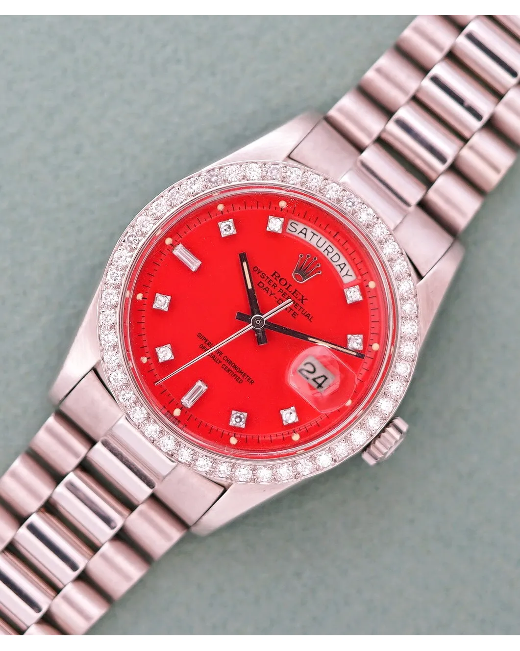 Dial detail of a Rolex Day-Date with red dial, diamond bezel, diamond hour markers, and President bracelet.