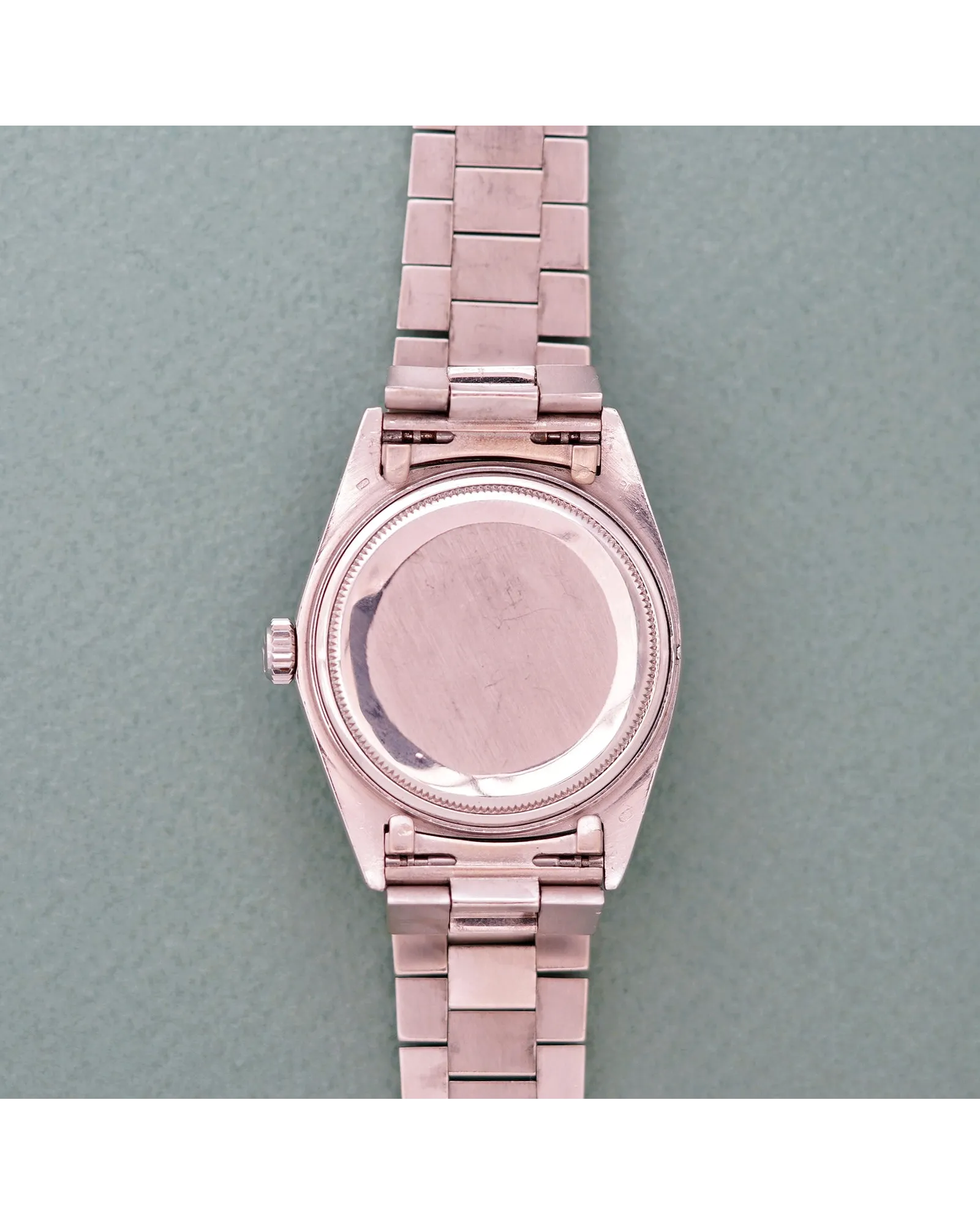Caseback view of a rose gold-toned watch with fluted bezel and three-link Oyster-style bracelet on grey surface.