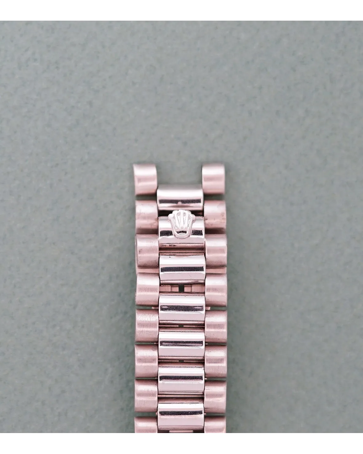 Bracelet detail of a rose gold Rolex President bracelet with crown-engraved clasp on grey background.