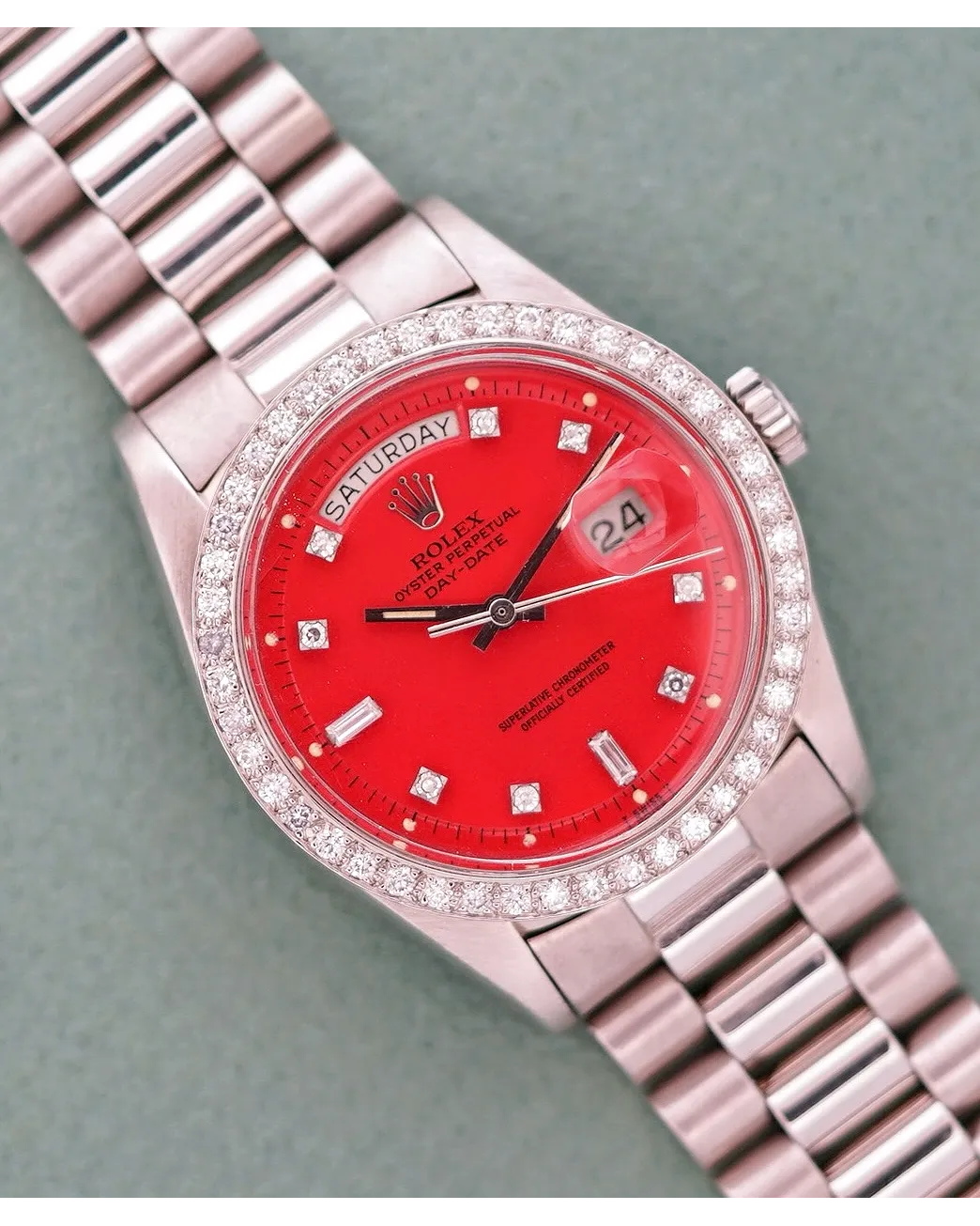 Dial detail of a Rolex Day-Date with red dial, diamond bezel, diamond hour markers, and President bracelet.