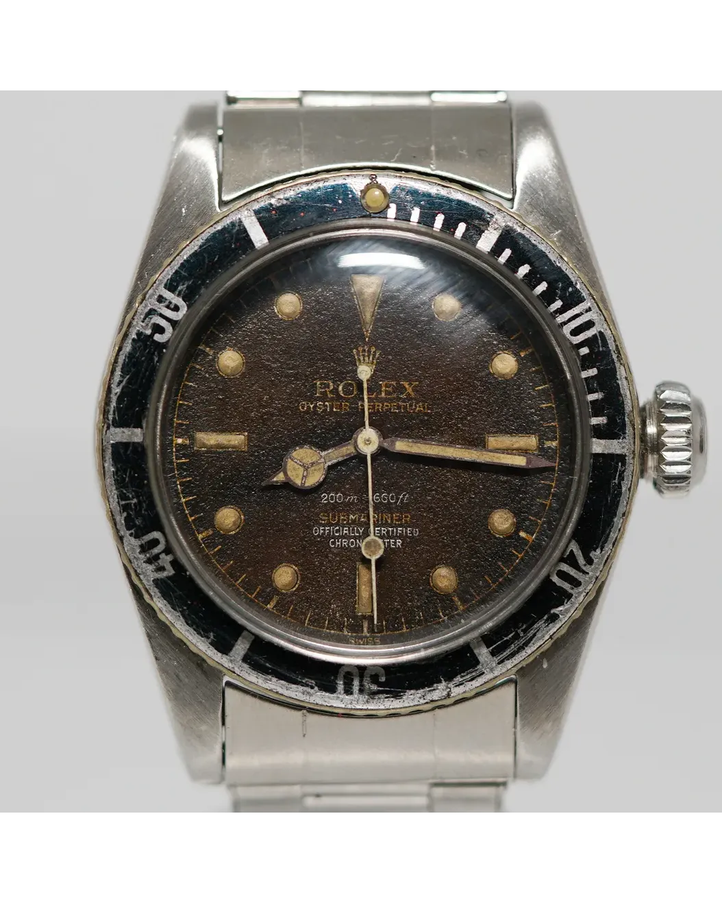 Dial detail of a Rolex Oyster Perpetual Submariner with tropical brown dial, gilt text, luminous hour markers, and worn rotating bezel on rivet bracelet.