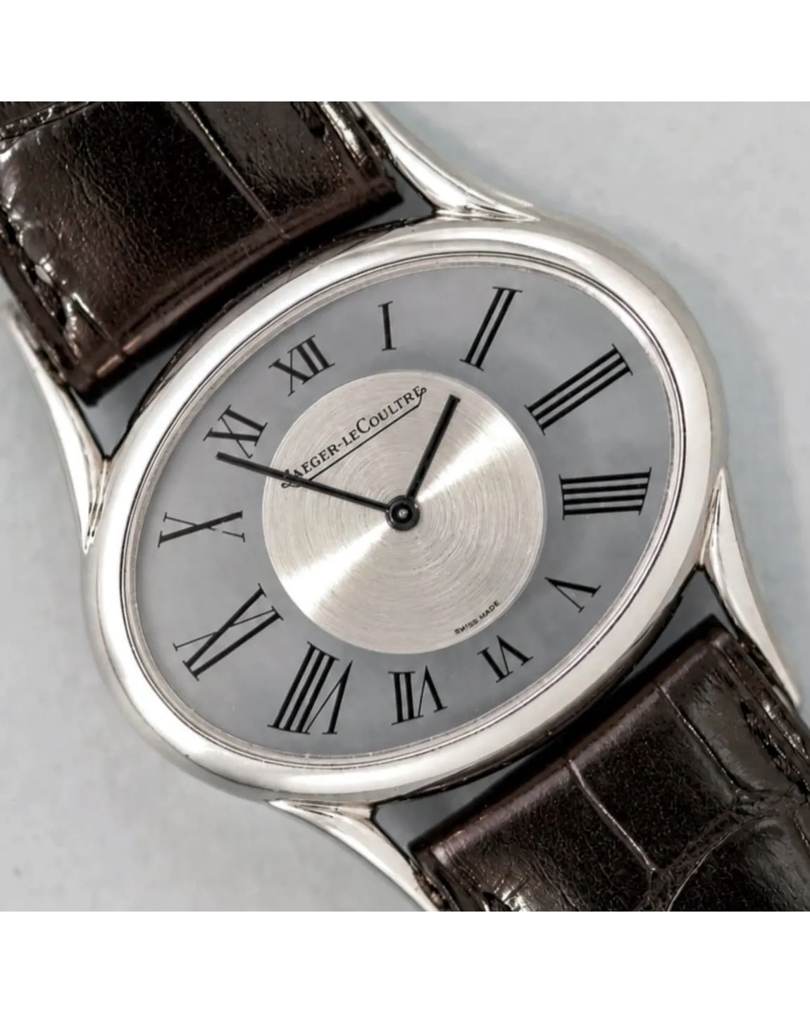 Dial detail of a Jaeger-LeCoultre dress watch featuring grey dial, Roman numerals, and brown alligator strap.