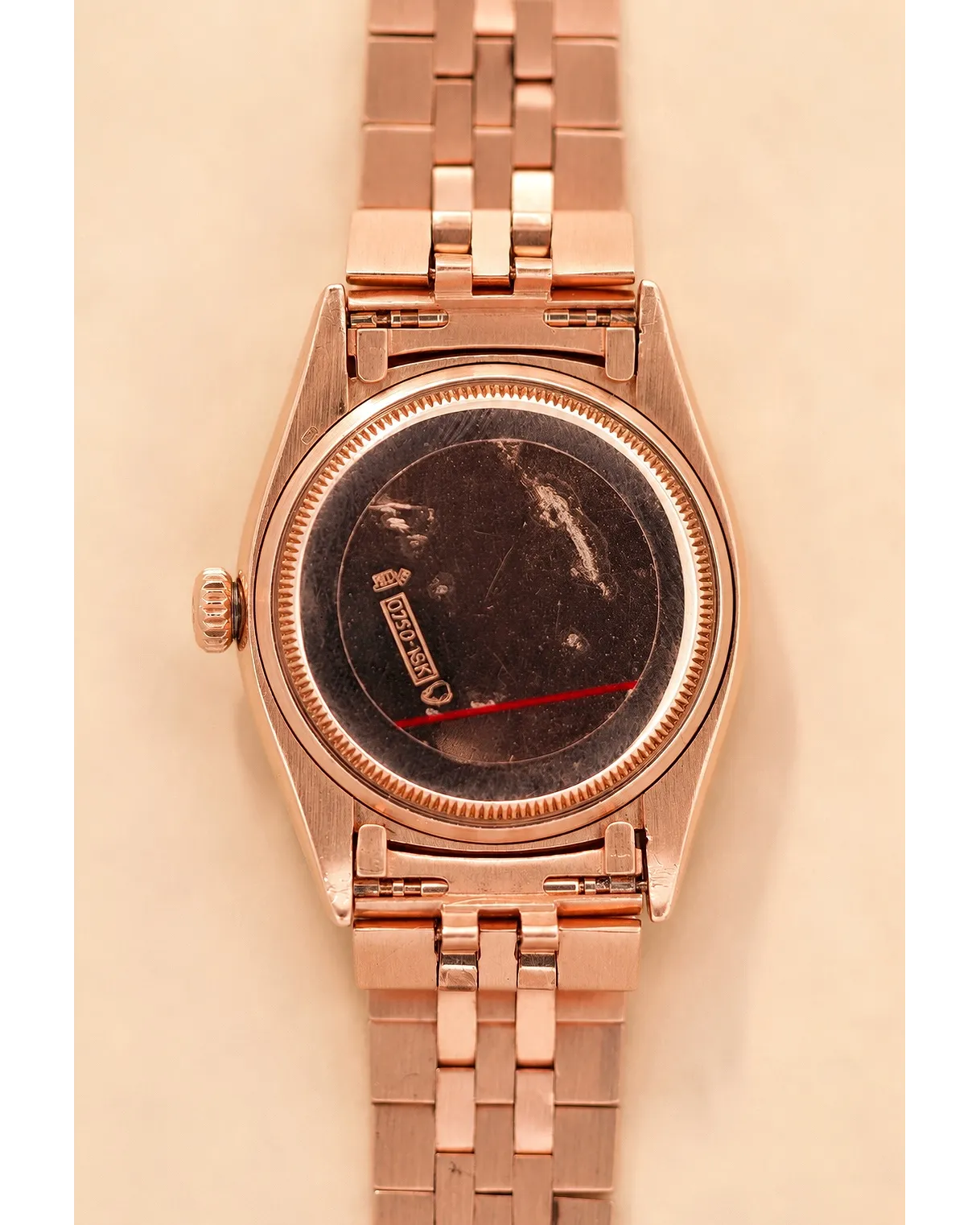 Caseback view of a rose gold-cased vintage watch with fluted bezel, red sweep hand, and Jubilee-style bracelet.