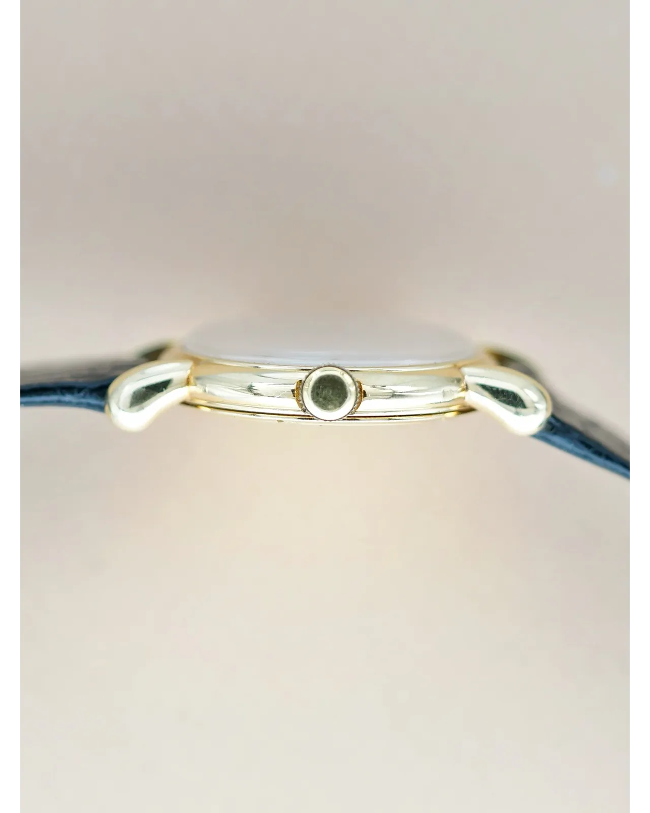 Profile shot of a gold-cased vintage dress watch with blue leather strap and smooth bezel.