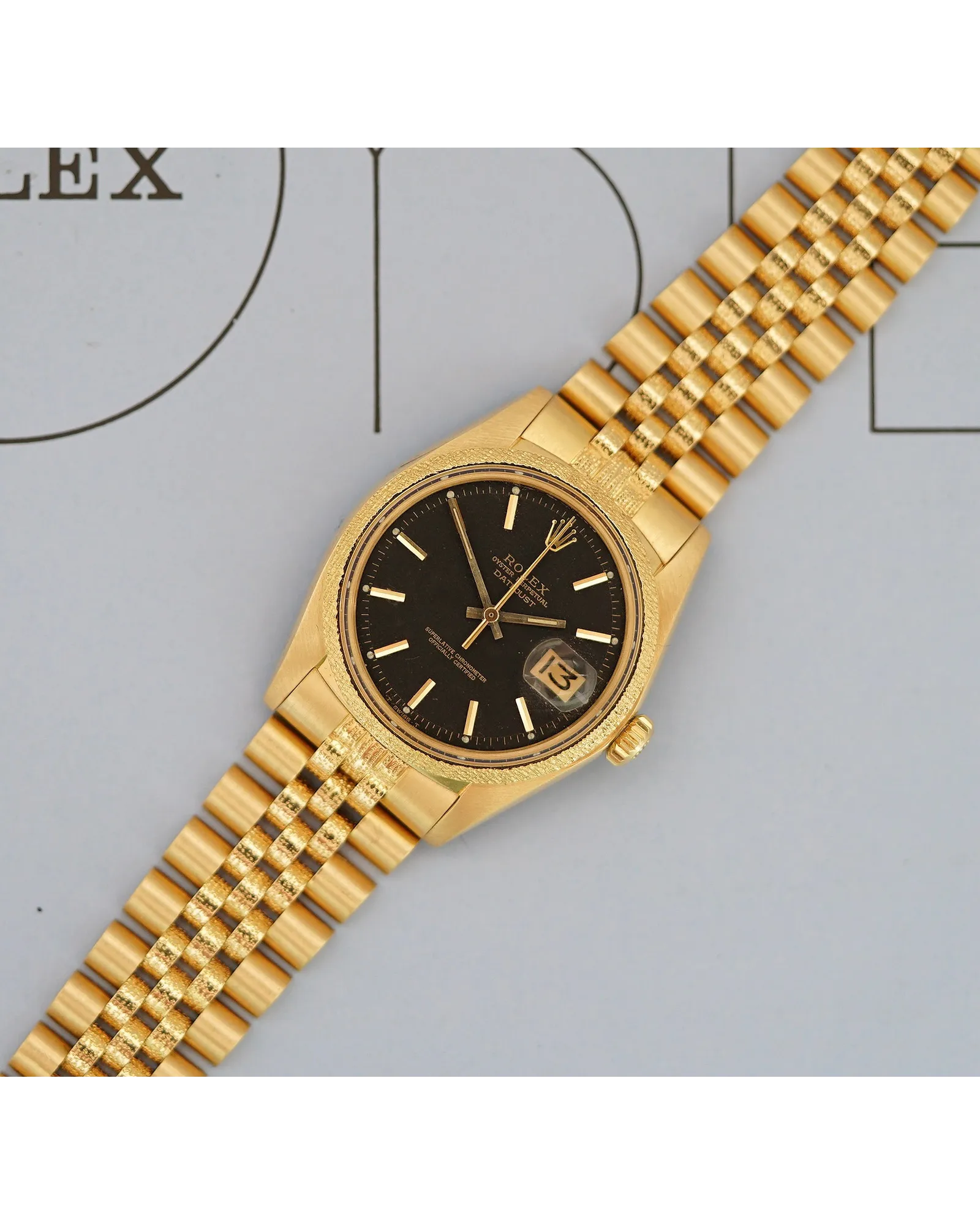 Flat-lay shot of a Rolex Datejust in yellow gold with black dial, baton indices, and Jubilee bracelet.