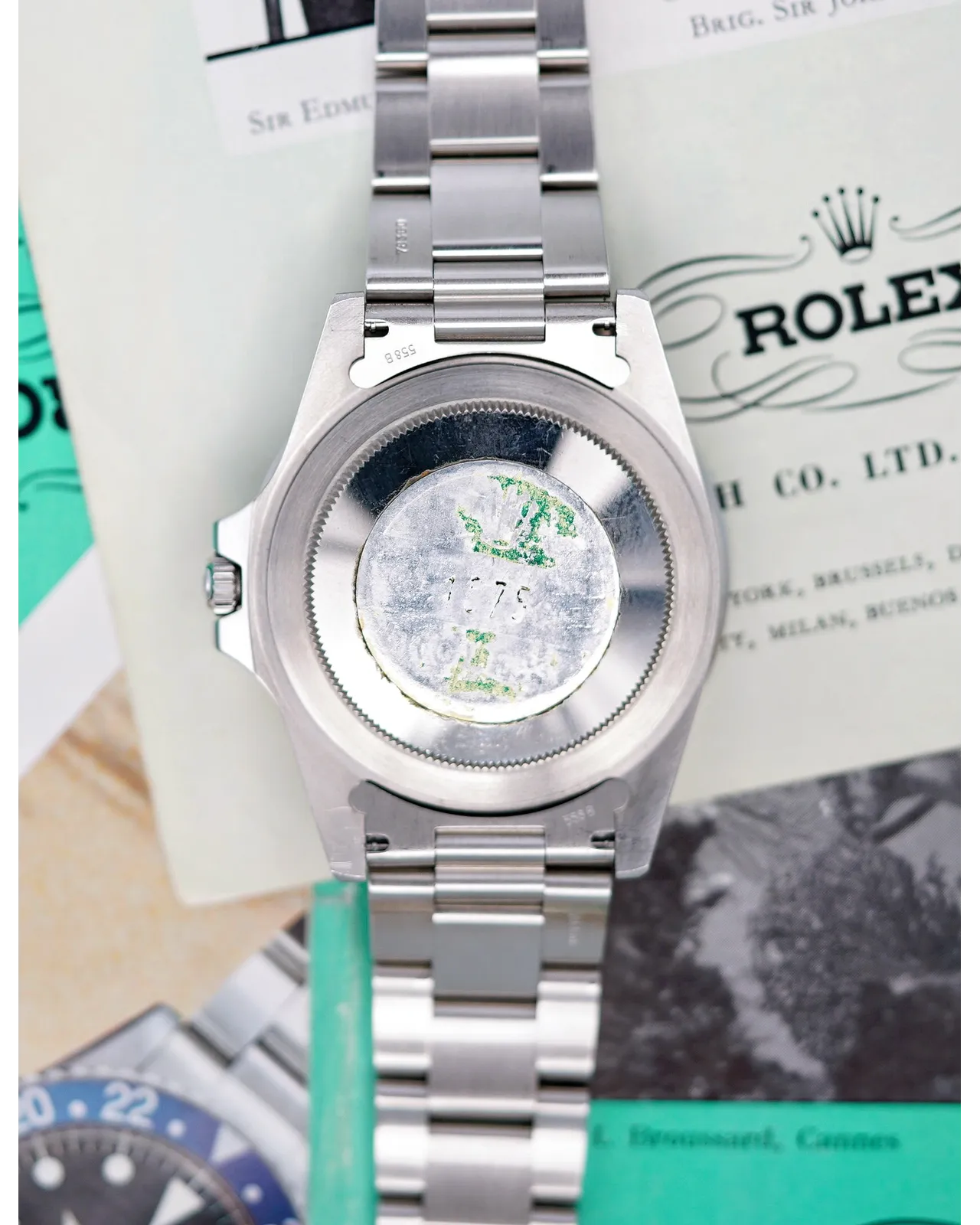 Caseback view of a Rolex Oyster Perpetual on stainless steel bracelet with original papers and green hangtag visible.