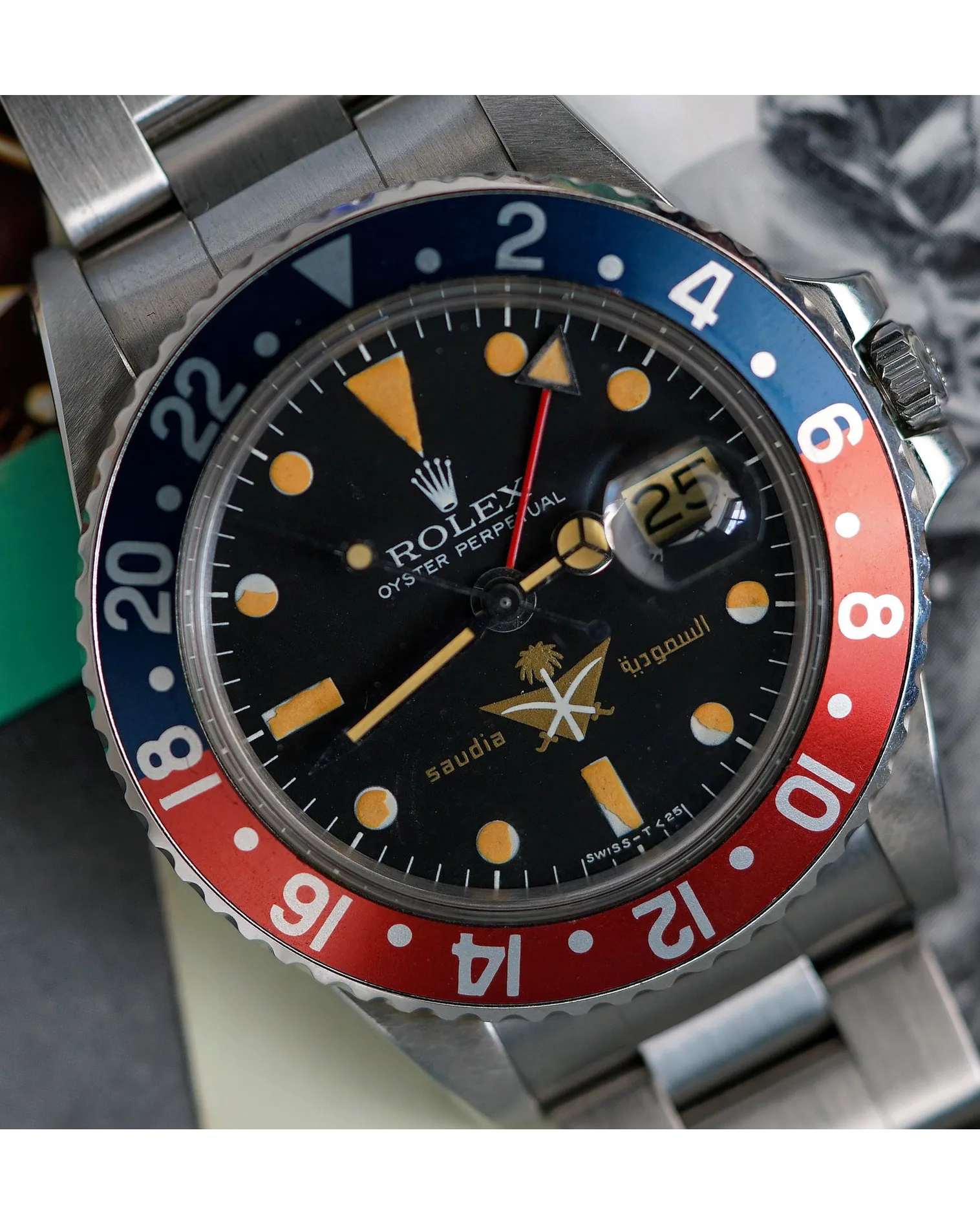 Dial detail of a Rolex GMT-Master with blue and red bezel, patinated luminous markers, and Saudi Arabian dial emblem.