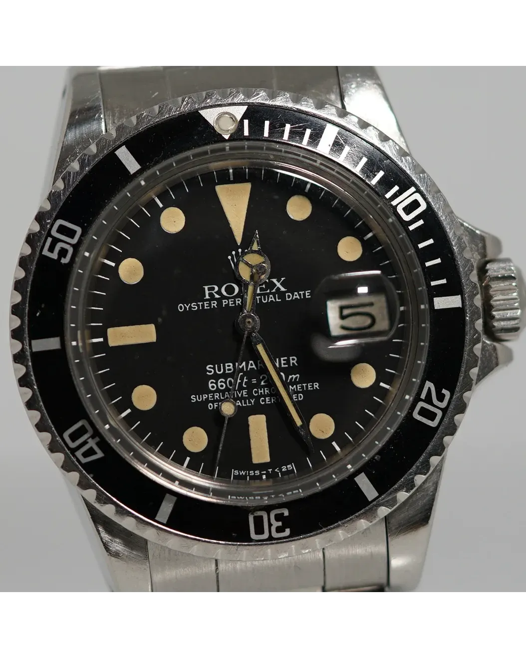 Dial detail of a Rolex Submariner Date with black matte dial, creamy patinated luminous markers, and date magnifier.