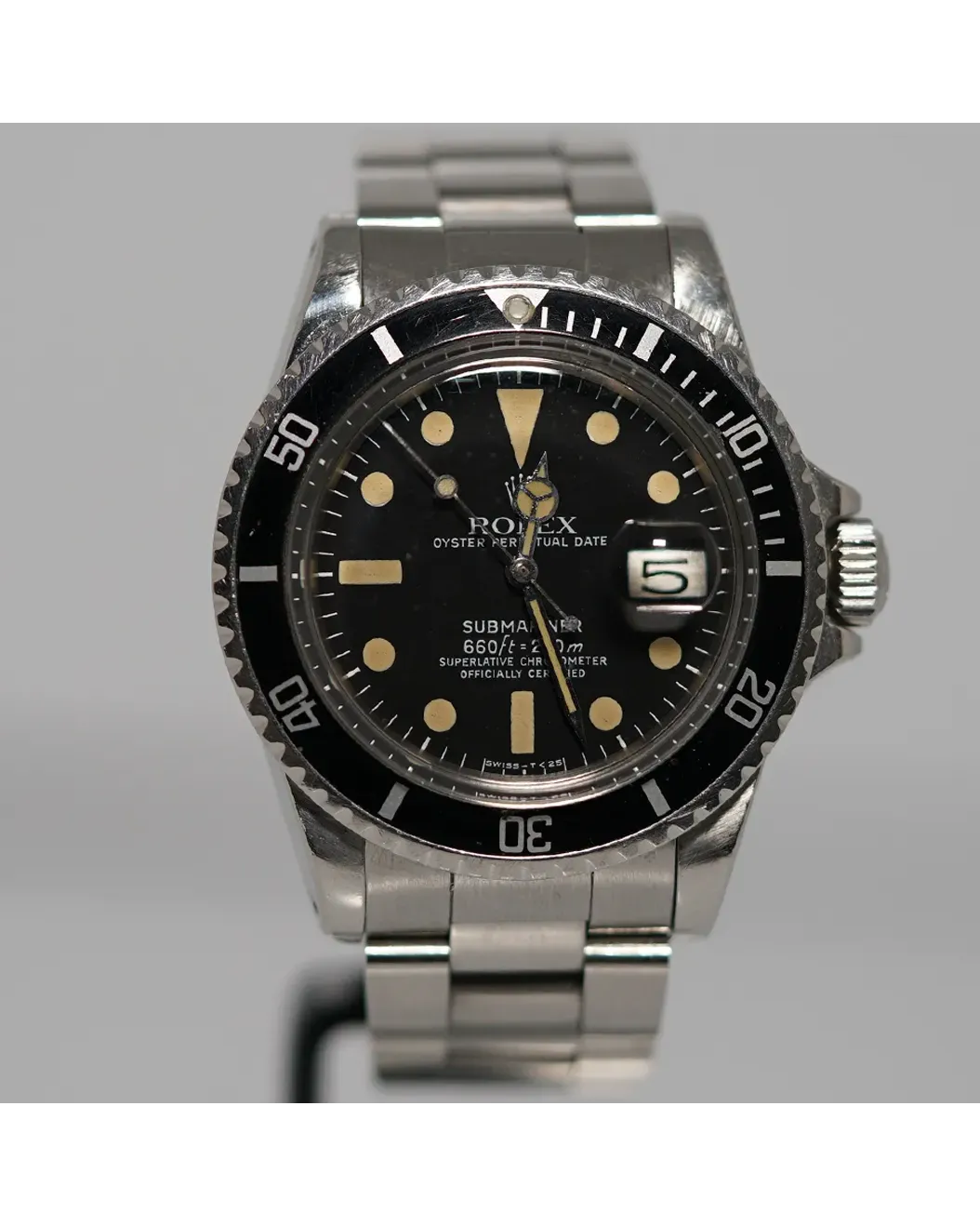 Dial view of a Rolex Submariner Date with black bezel, aged tritium markers, and steel bracelet.