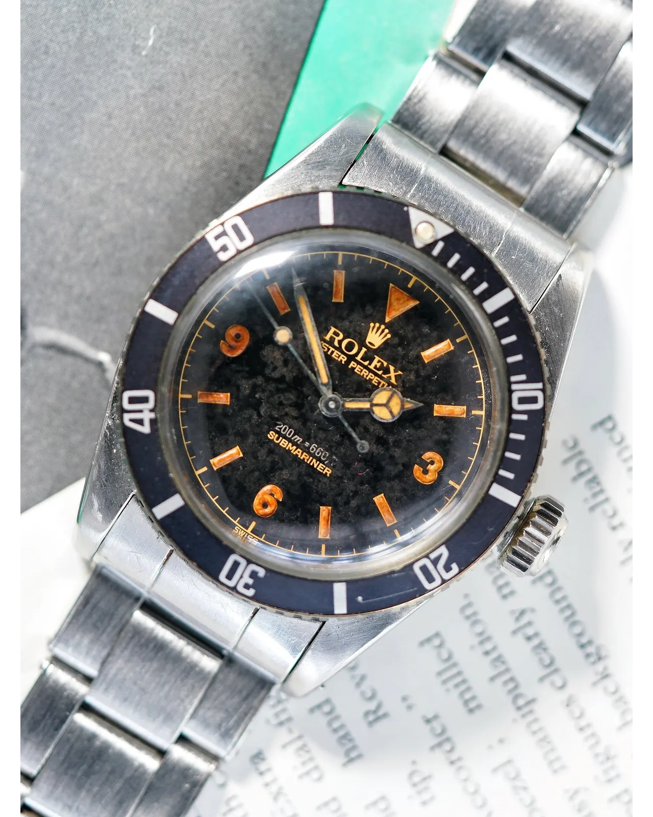Dial detail of a vintage Rolex Submariner showing black tropical dial with orange patina and blue bezel insert.