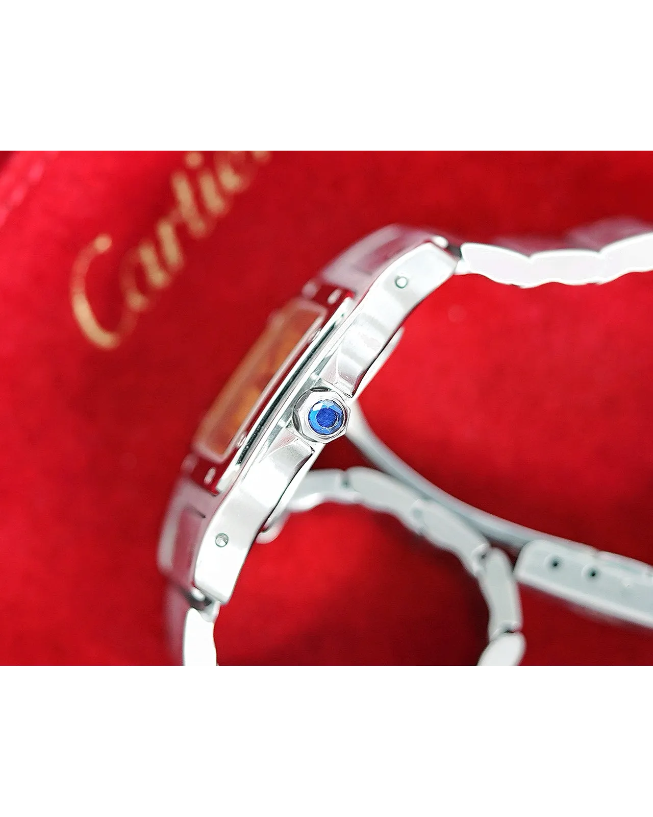 Profile shot of a Cartier watch showing polished steel case with blue cabochon crown and bracelet.