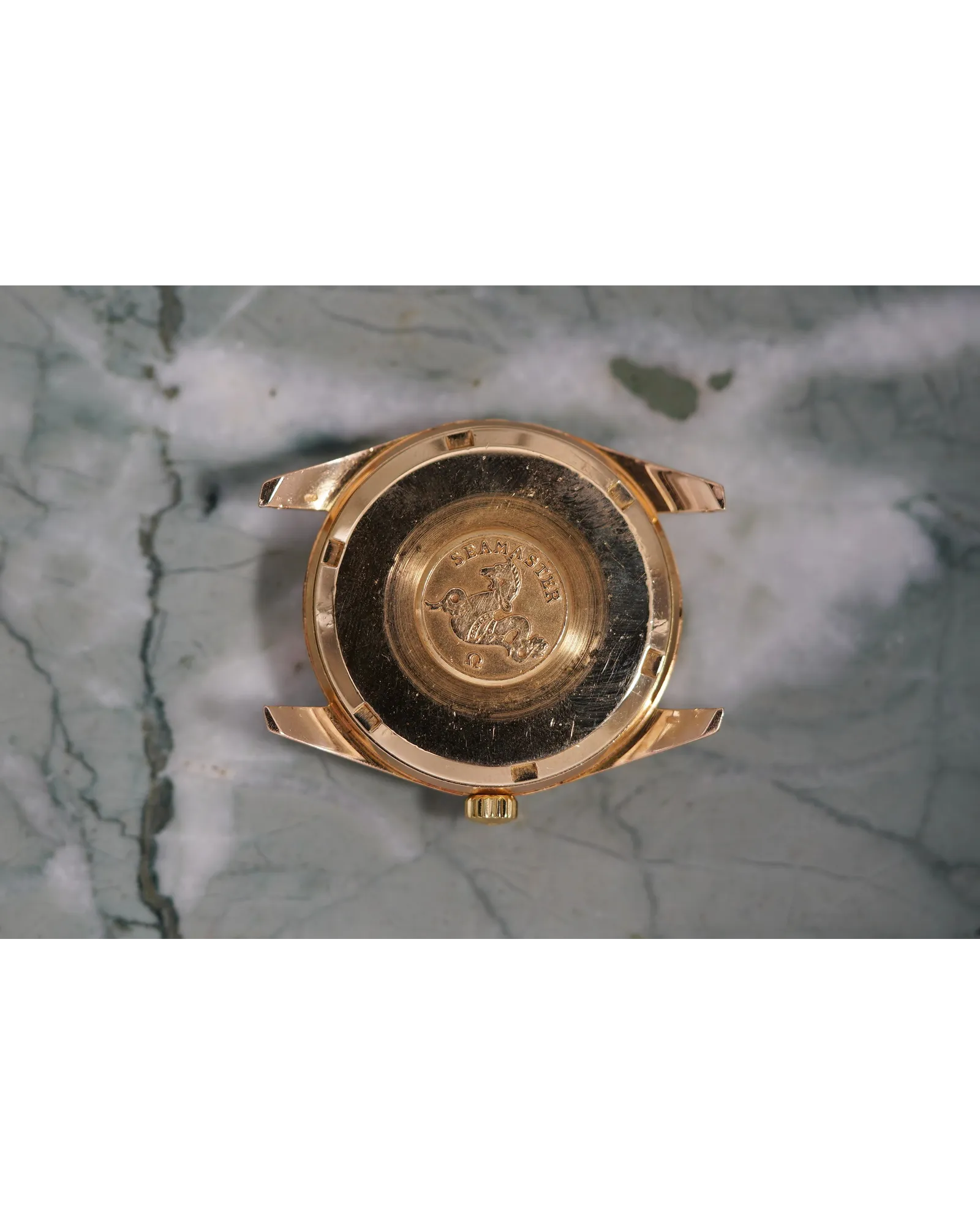 Caseback view of a rose gold Omega Seamaster with hippocampus emblem and circular brushed finish.