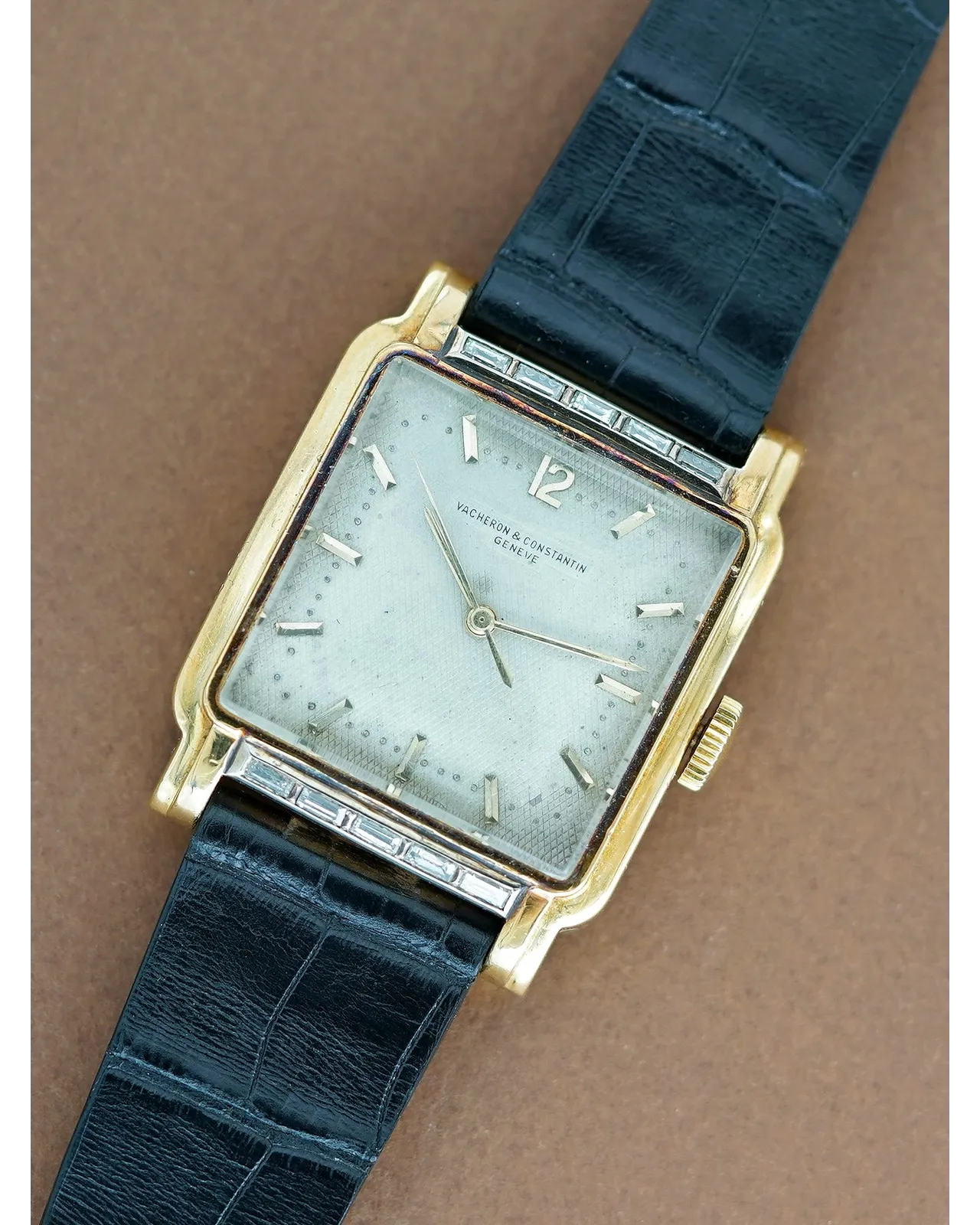 Dial view of a Vacheron Constantin rectangular yellow gold watch with silvered dial, applied markers, and baguette diamond bezel on black leather strap.