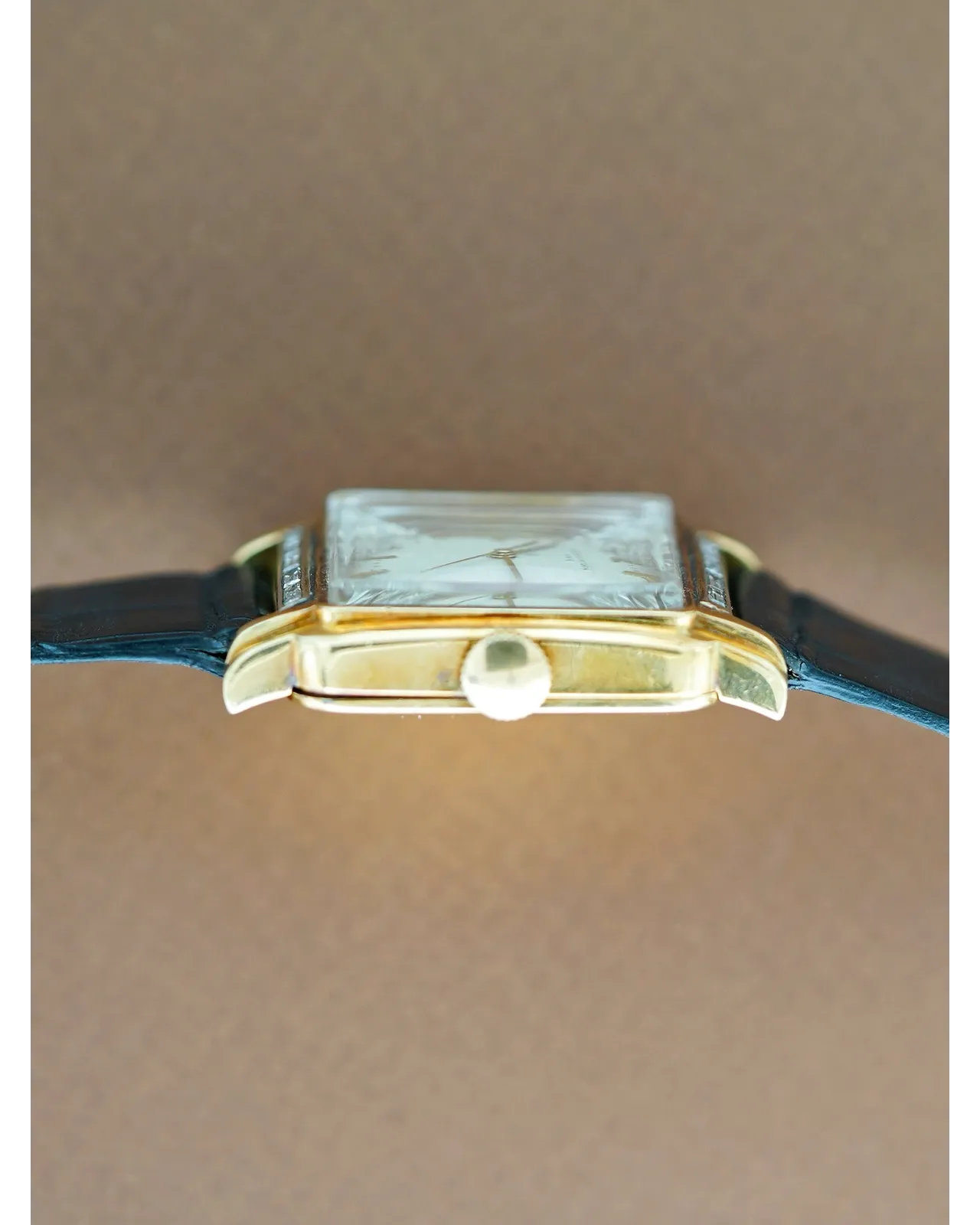 Profile shot of a rectangular gold-cased dress watch with silvered dial on dark blue leather strap.