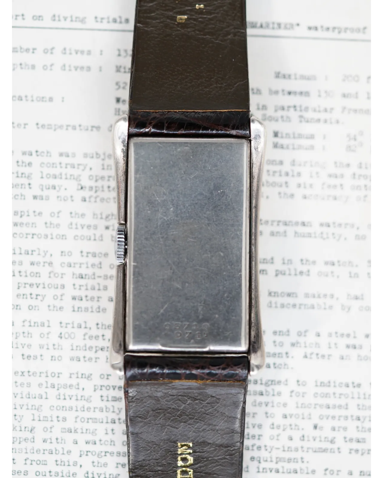 Caseback view of a rectangular dress watch with stepped steel case on brown leather strap.