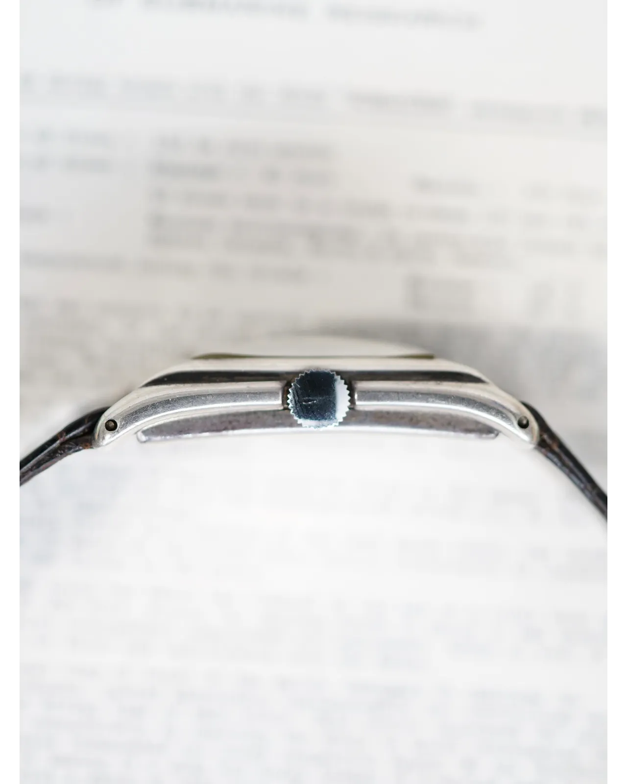 Profile shot of a slim stainless steel wristwatch with blue crown on black leather strap.