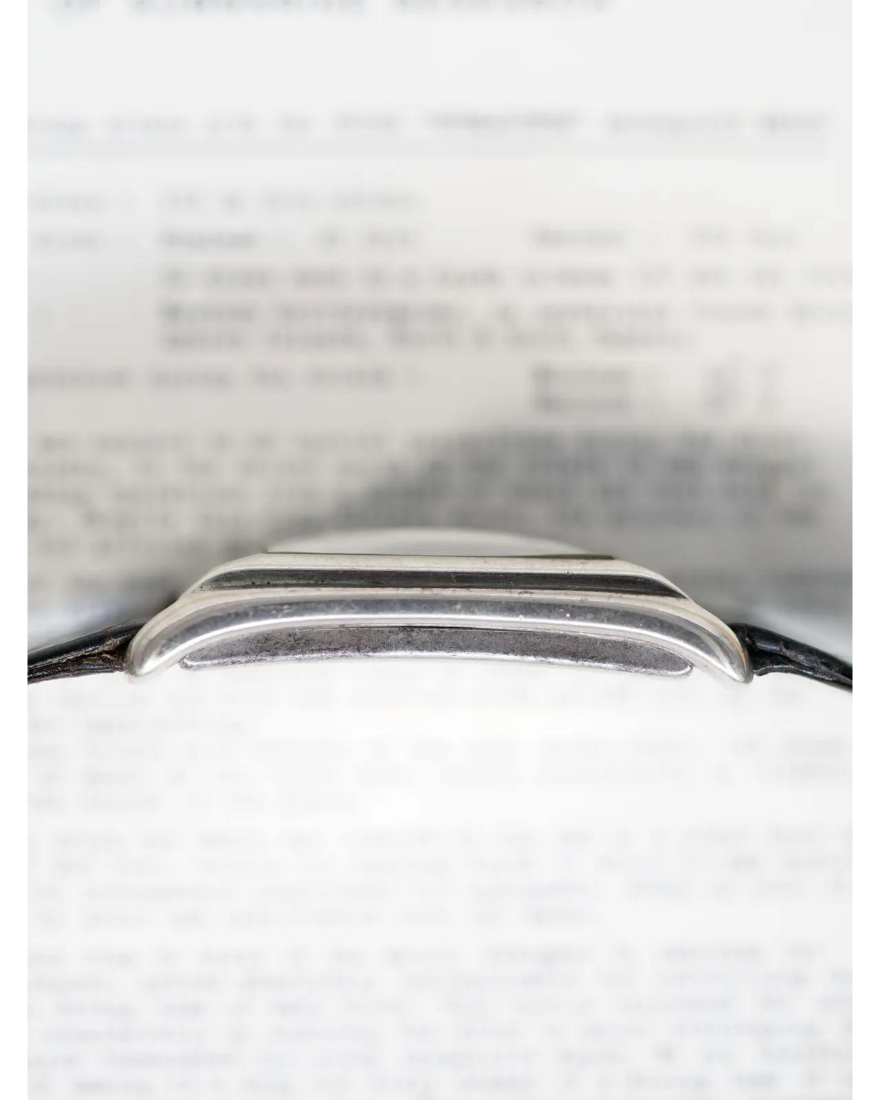 Profile shot of a vintage watch case showing polished stepped lugs and black leather strap.