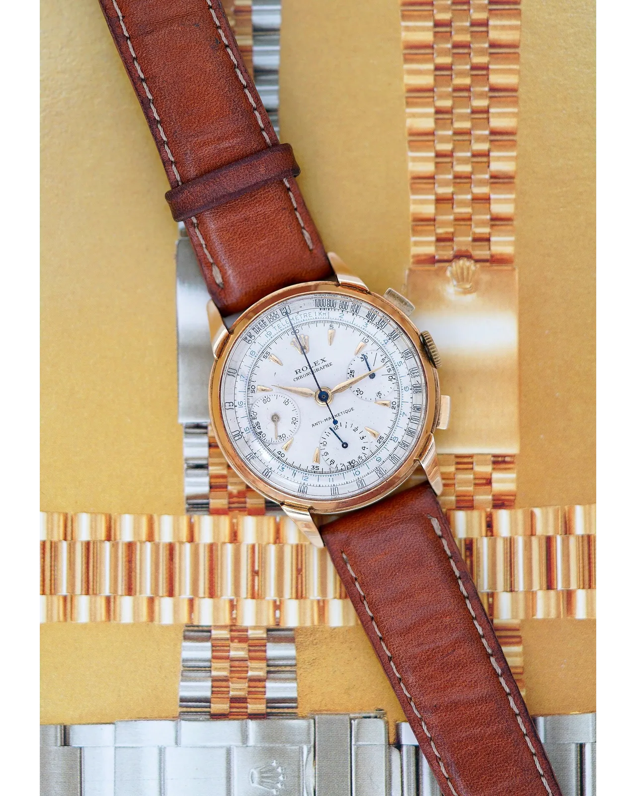 Dial detail of a Rolex chronograph in rose gold with anti-magnetic designation on brown leather strap.